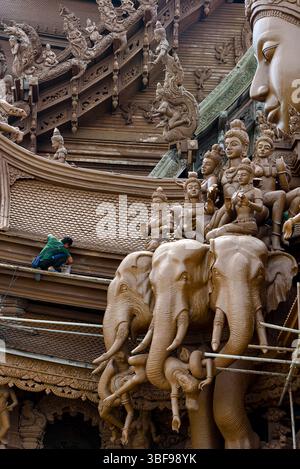 Lavoratore che lavora al Santuario della verità, Pattaya, Thailandia. Costruito e scolpito in teak. Il Santuario della verità a Pattaya, Thailandia, è una monumentale struttura in legno che mescola stili architettonici thailandesi, indù, buddisti, cinesi e Khmer. Iniziato nel 1981 da un uomo d'affari, il santuario è costruito interamente in teak e altri legni duri senza chiodi metallici. Alto 105 metri e alto 2.115 metri, presenta intricate incisioni raffiguranti filosofie orientali e temi religiosi. Anche se ancora in costruzione, rimane un significativo punto di riferimento culturale e spirituale Foto Stock