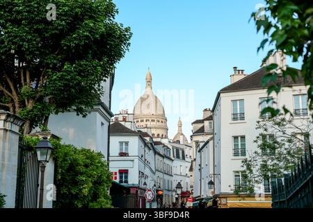 Una vista pittoresca della Basilica del Sacro Cœur che si erge sopra gli edifici di Montmartre, Parigi, incorniciata naturalmente da alberi verdi e da una linea scura di recinzione. Foto Stock