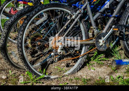 Primo piano della ruota posteriore di una biycycle deserta arrugginita in un affollato portabiciclette blu al sole Foto Stock