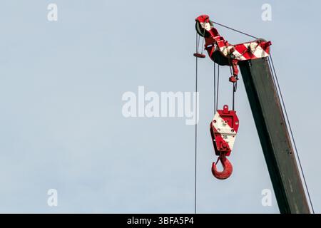 Un gancio rosso brillante su un braccio di gru da costruzione contro un cielo limpido. Questa immagine cattura l'essenza dei macchinari industriali in azione, mostrando i suoi Foto Stock