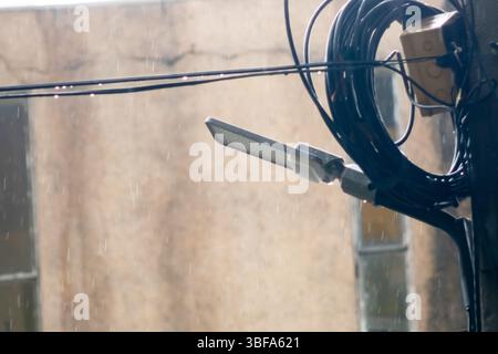 Vista ravvicinata di un lampione in mezzo alla pioggia in caduta, con cavi elettrici in alto. La scena cattura l'ambiente urbano in una giornata cupa, evoki Foto Stock