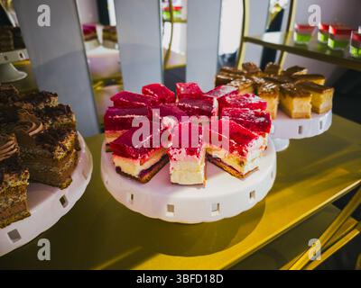 Torte gourmet assortite su banchi bianchi in un'elegante esposizione di dessert Foto Stock