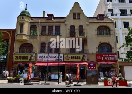 Edificio in stile coloniale tedesco con una torretta decorativa ora occupata da moderni negozi cinesi con cartelli cinesi a Qingdao, Shandong, Cina Foto Stock