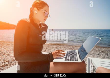 Donna laptop Beach lavora in remoto - la giovane donna lavora con un notebook mentre si rilassa in spiaggia. Foto Stock