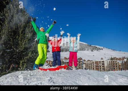 I bambini saltano con gioia sulle piste da sci spargendo neve bianca fresca Foto Stock