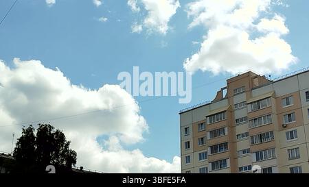 Vista dal basso dei piani superiori della facciata dell'edificio sullo sfondo di nuvole volanti in un cielo blu soleggiato. Foto Stock