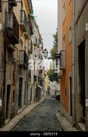 Una stretta strada lastricata nel quartiere Alfama di Lisbona, Portogallo. La strada è fiancheggiata da edifici antichi costruiti con pietra e mattoni, esposti Foto Stock