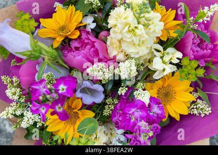 Bouquet di fiori avvolti di fiori primaverili misti. Splendidi fiori freschi dai colori vivaci. Bouquet di compleanno con peonie e girasoli Foto Stock