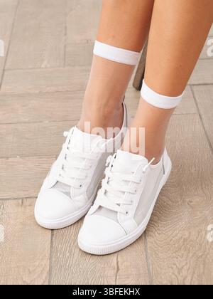 Eleganti sneakers bianche sui piedi di una persona appoggiate su un pavimento in legno in piena luce Foto Stock