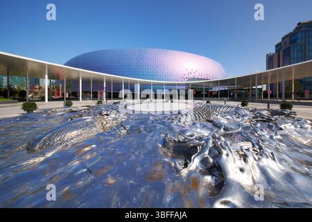 Kai Tak, Hong Kong - 12 maggio 2025: Kai Tak Stadium e Central Square, con nove draghi parziali, opera d'arte (centrata) della piazza, in primo piano. Foto Stock