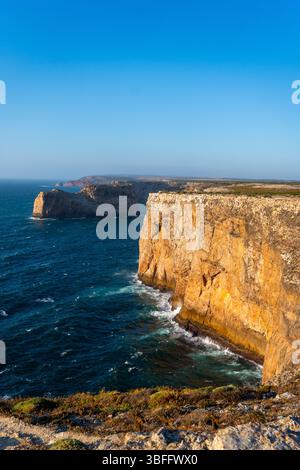 Un'ampia ripresa verticale che cattura la grande scala delle scogliere dorate di Cabo da Roca che si tuffano nel blu profondo dell'Oceano Atlantico sotto un luminoso c Foto Stock
