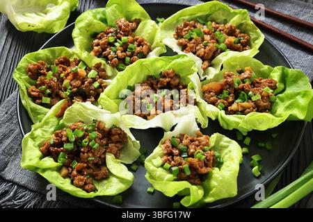 Tazze di lattuga di pollo macinato fresco e croccante di lattuga bibb, pollo macinato, spezie, salsa hoisin e soia su un piatto su un tavolo di legno nero, horiz Foto Stock