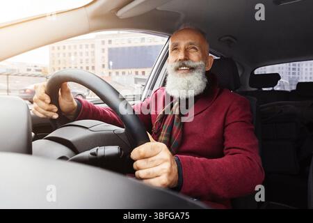 Bell'anziano uomo dai capelli grigi seduto all'interno di una nuova auto, che viaggia da solo Foto Stock