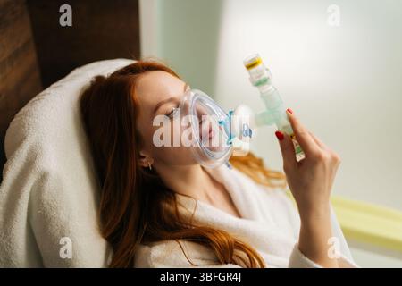 Primo piano di una paziente malata rossa che indossa una maschera di ossigeno collegata al tubo, respirando con difficoltà, durante la terapia respiratoria in Foto Stock