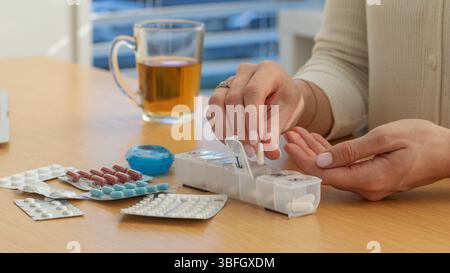 Donna adulta che mette medicinali in pillbox sul tavolo. Mani femminili che mettono pillole in contenitori di plastica Foto Stock