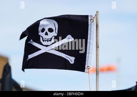 Bandiera dei pirati che sventola contro un cielo azzurro trasparente su un palo di legno. Hayling Island, Regno Unito Foto Stock