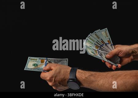 Due mani stanno scambiando una pila di contanti in un ambiente poco illuminato. L'attenzione è rivolta al denaro e alle mani coinvolte nella transazione. Foto Stock