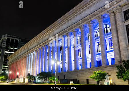 Vista notturna del New York State Education Building ad Albany con il suo lungo colonnato corinzio, illuminato in blu e rosso. La facciata Beaux-Arts si erge contro un cielo scuro, creando un contrasto sorprendente con gli archi illuminati, i capitelli ornati e la ripetizione ritmica delle colonne lungo l'ampia strada Foto Stock