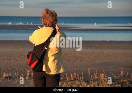 Donna matura in piedi sulla spiaggia e a scattare foto Foto Stock