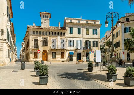 Stretta strada acciottolata e architettura storica su una piccola piazza della città sotto un cielo blu nella città vecchia di Mahon, Minorca, Spagna. Foto Stock