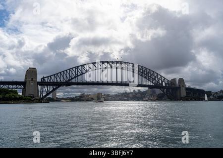 Il Sydney Harbour Bridge di Sydney, Australia, si estende attraverso il porto sotto un cielo nuvoloso. Il ponte ad arco d'acciaio collega la città, offrendo un'atmosfera mozzafiato Foto Stock