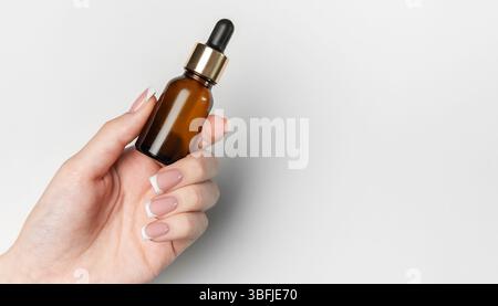 L'estetista tiene in mano il flacone contagocce in vetro ambrato con elementi dorati su sfondo bianco e spazio di copia Foto Stock