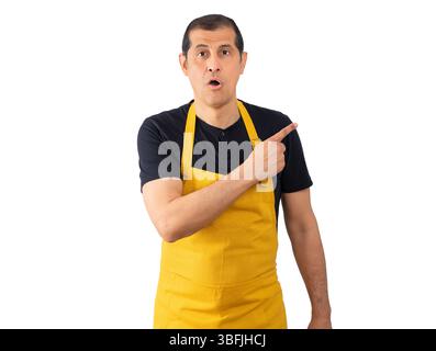 Bell'uomo che indossa il grembiule del dipendente su sfondo isolato. Sorpreso a puntare il dito verso un lato, bocca aperta espressione stupita. Foto Stock