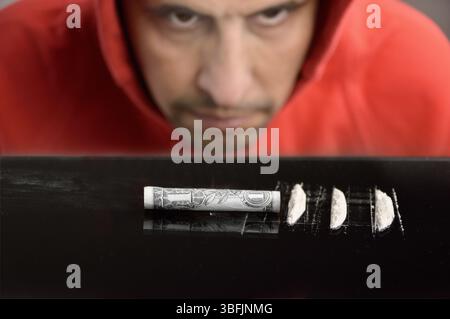 Primo piano di tossicodipendenti con cappuccio che guarda le strisce di cocaina sul tavolo nero Foto Stock