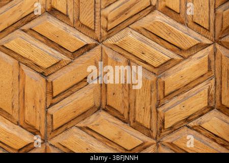 Primo piano dettagliato di una superficie decorativa in legno caratterizzata da un motivo geometrico con ricche texture in legno, che enfatizzano i toni naturali e la maestria artigianale. Foto Stock