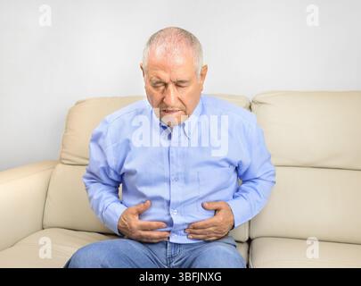 L'anziano soffre di mal di stomaco seduto su un divano nel salotto di casa Foto Stock