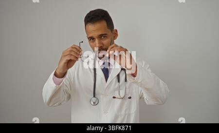 Ispanico maschio medico regolazione occhiali isolati su sfondo bianco in abbigliamento medico che sembra focalizzato. Foto Stock