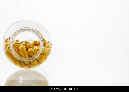 Un vaso con le pillole all'interno giace su uno sfondo bianco. Acido ialuronico, collagene, vitamine o mirtillo per perdere peso. Preparazioni mediche per la salute Foto Stock