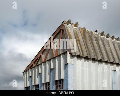 Dettagli architettonici ravvicinati di un edificio industriale in disuso con tetto e facciata in cemento con colonne di colore a contrasto Foto Stock