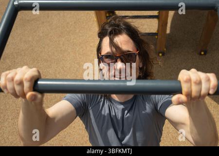 Uomo che indossa occhiali da sole che fa il tifo per scimmie all'aperto, concentrato sull'attività fisica. Ambiente soleggiato all'aperto. Primo piano. Foto Stock