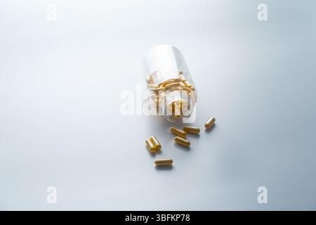 Un vaso con le pillole all'interno giace su uno sfondo bianco. Acido ialuronico, collagene, vitamine o mirtillo per perdere peso. Preparazioni mediche per la salute Foto Stock