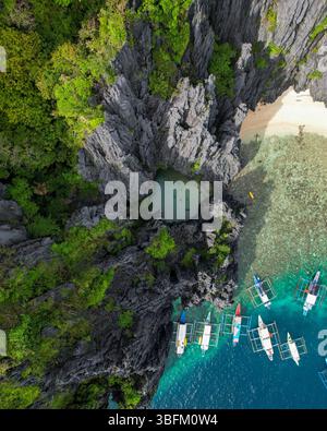 Vista aerea di una spiaggia nascosta circondata da colline calcaree, acque turchesi e barche ancorate a El Nido, Palawan. Un paradiso tropicale Foto Stock