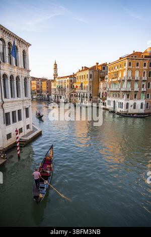 Vista del Canal grande con i gondolieri al tramonto, atmosfera serale pittoresca con i palazzi sul canale e la torre della chiesa parrocchiale dei Foto Stock