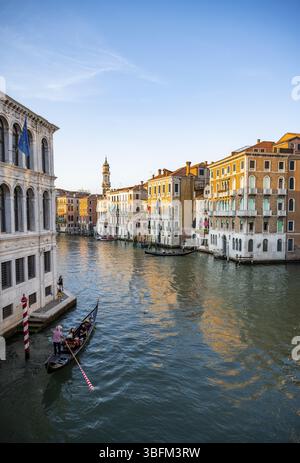 Vista del Canal grande con i gondolieri al tramonto, atmosfera serale pittoresca con i palazzi sul canale e la torre della chiesa parrocchiale dei Foto Stock