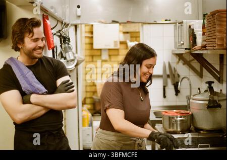 Donna sorridente che cucina il cibo mentre si trova accanto all'uomo nella cucina del ristorante Foto Stock