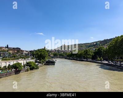 Vista del fiume Kura e del paesaggio urbano di Tbilisi dal Peace Bridge in una soleggiata giornata estiva in Georgia. Niente persone. Foto Stock
