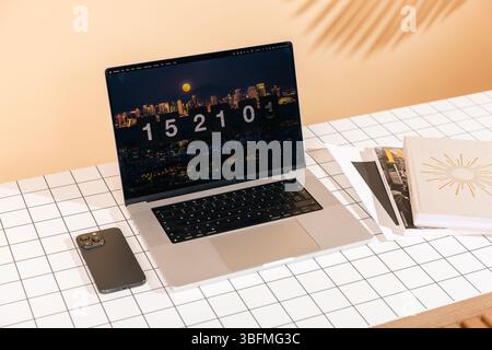 Uno spazio di lavoro contemporaneo con un laptop che visualizza una scena notturna della città con uno screensaver con orologio a scatto, insieme a uno smartphone e a libri su una griglia pa Foto Stock