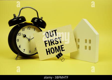 Il nostro primo messaggio Home con modello di casa e sveglia su sfondo giallo Foto Stock
