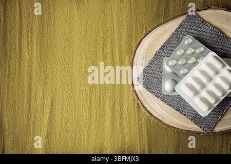 Posizione piatta minima con confezioni blister di capsule e compresse su vassoio di legno e tessuto testurizzato. Luce naturale e concetto pulito per il benessere, ogni giorno Foto Stock