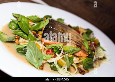 Viene servito un piatto di salmone, caratterizzato da basilico, pomodori e peperoni, offrendo un'esperienza culinaria fresca e saporita. Foto Stock