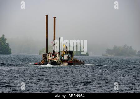 tugboat che sposta una chiatta lungo il fiume St. Lawrence nella nebbia mattutina. Foto Stock