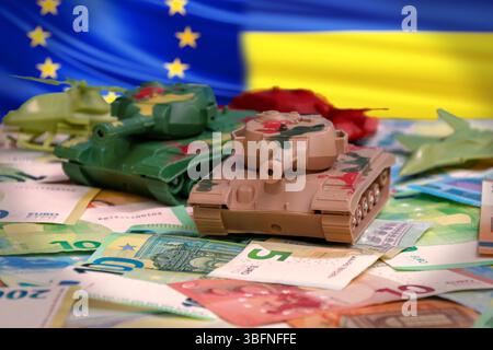 Aiuti militari dell'Unione europea all'Ucraina. Le cisterne giocattolo e l'aviazione sullo sfondo delle bandiere UE e Ucraina sulle banconote in euro simboleggiano i finanziamenti per la difesa e gli stagisti Foto Stock