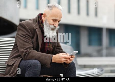 Felice uomo anziano che usa lo smartphone mentre riposa sulla strada Foto Stock