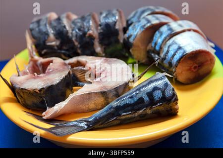 Piastra con fette di sgombro appena tagliato disposte a fianco di filetti interi con code intatte. Colore e consistenza naturali del pesce Foto Stock