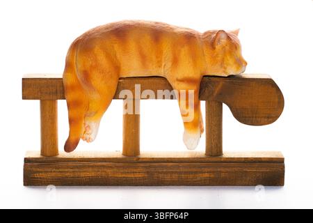 Un'affascinante statuetta di gatto allo zenzero che dorme tranquillamente drappeggiata su un rustico piedistallo in legno. Isolata sul bianco, perfetta per temi di relax, comfort, Foto Stock
