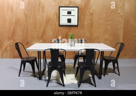 Mettiamo tutto sul tavolo: Tavolo in cemento con sei sedie in metallo in un capannone con opere d'arte sulla parete di legno Foto Stock